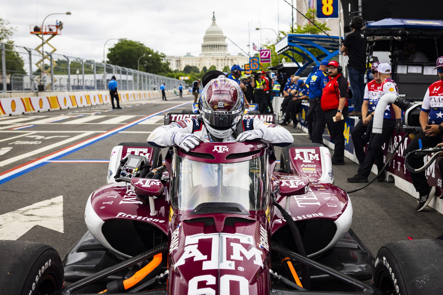 The maroon Texas A&M IndyCar of Felix Rosenqvist on pit lane, with the U.S. Capitol in the distance