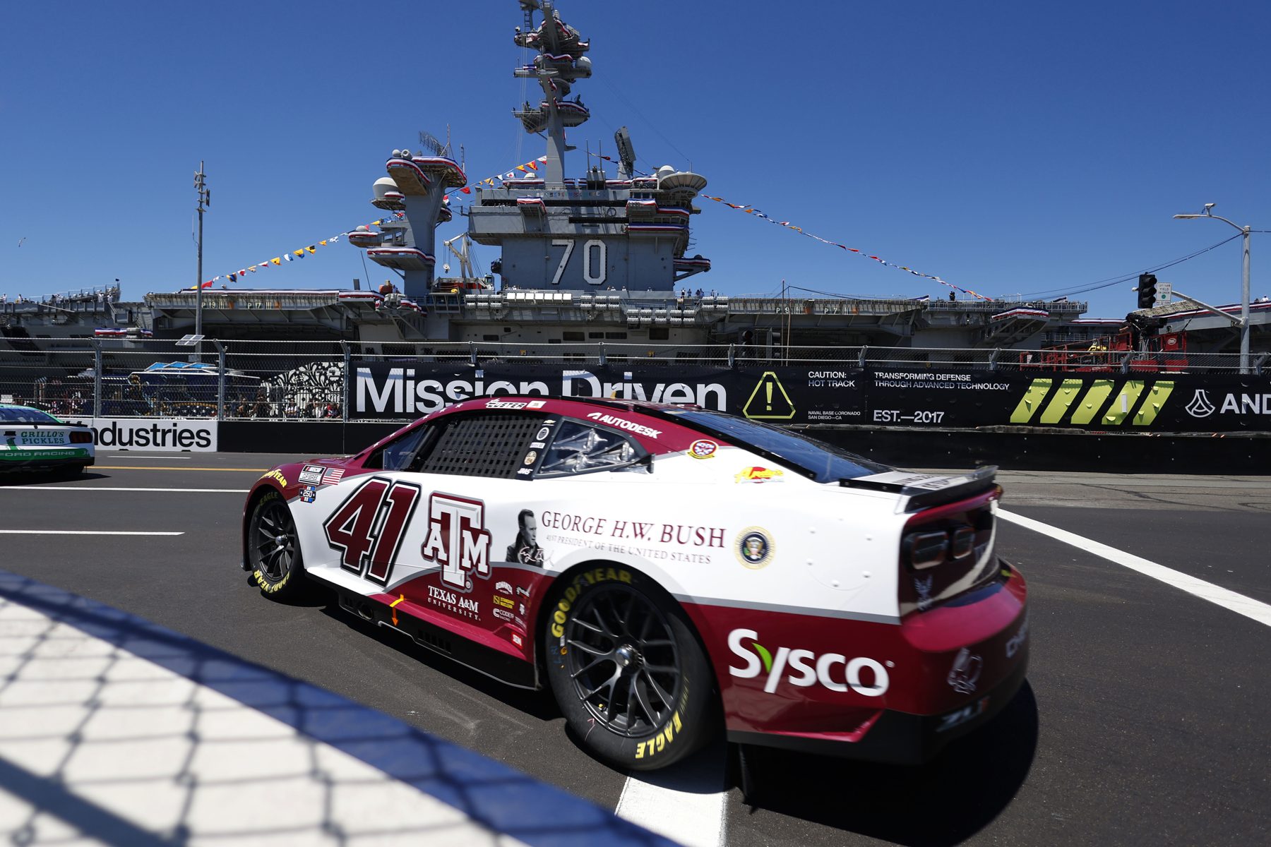 The maroon and white Texas A&M No. 41 Chevrolet, carrying a George H.W. Bush tribute, passing an aircraft carrier at Naval Base Coronado